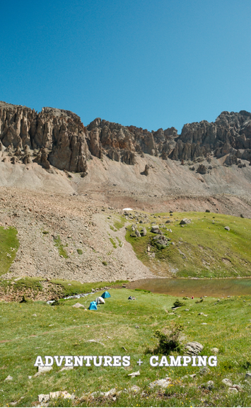 Green field by lake surrounded by mountains with tents.