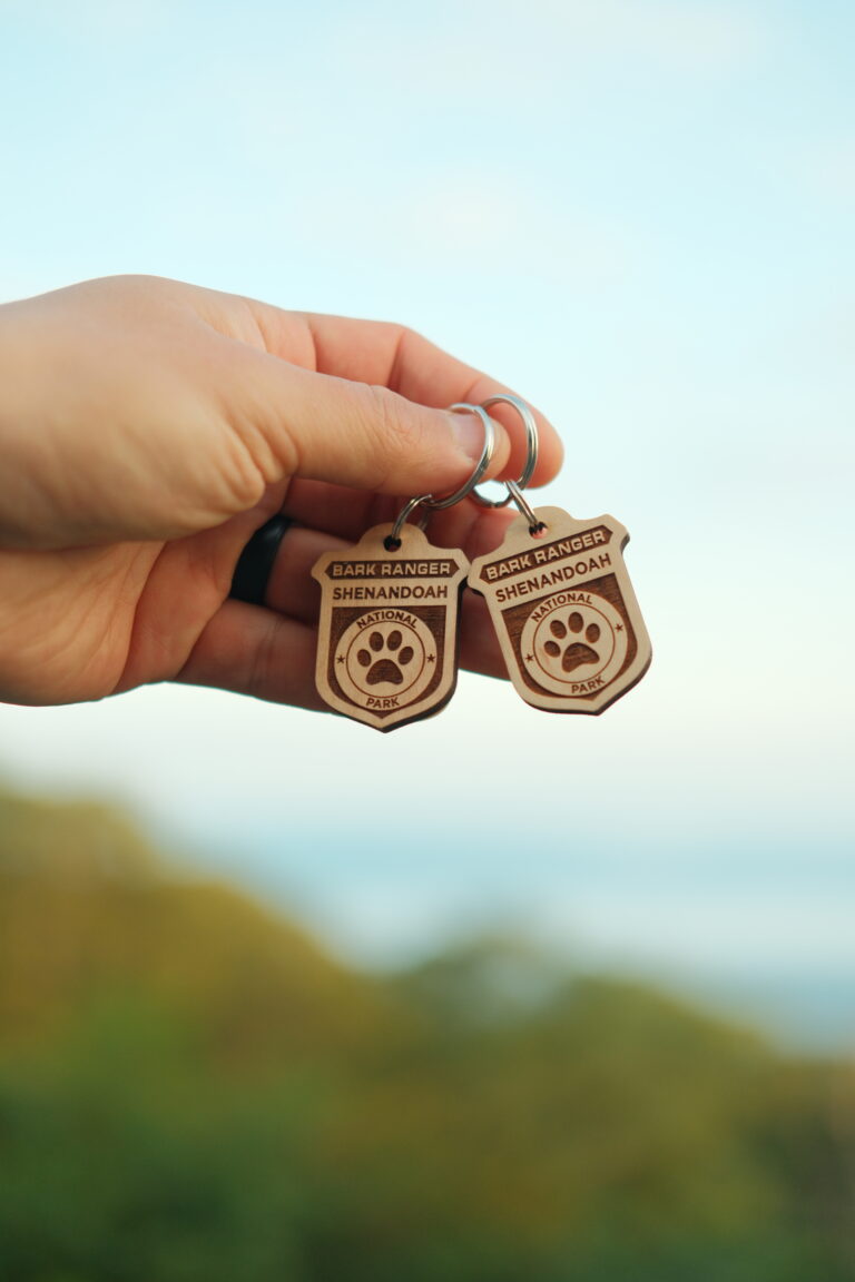 A hand is holding up 2 wooden keychains that read Shenandoah Bark Ranger